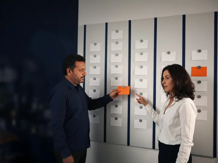 Consultor e dona de empresa movendo cartões num quadro com as etapas do funil comercial