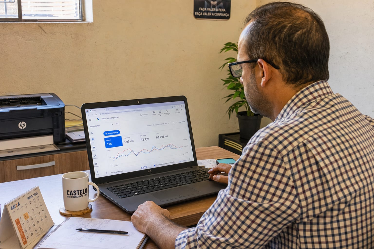 Dono de empresa em escritório de bairro no Castelo, BH, analisando o painel de campanhas do Google Ads no notebook com uma xícara de café ao lado